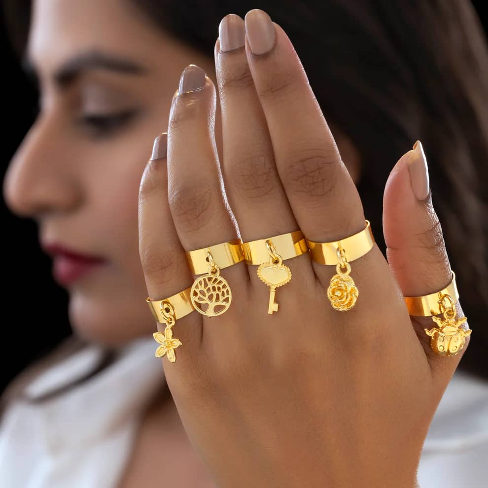 A woman's hand wearing a stack of five dainty gold charm rings from Ushve, her face softly out of focus behind